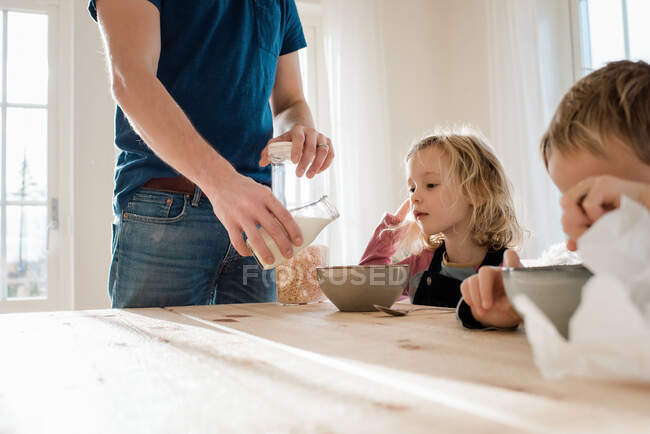 Padre ayudando a los niños con su desayuno en la mañana en casa - foto de stock