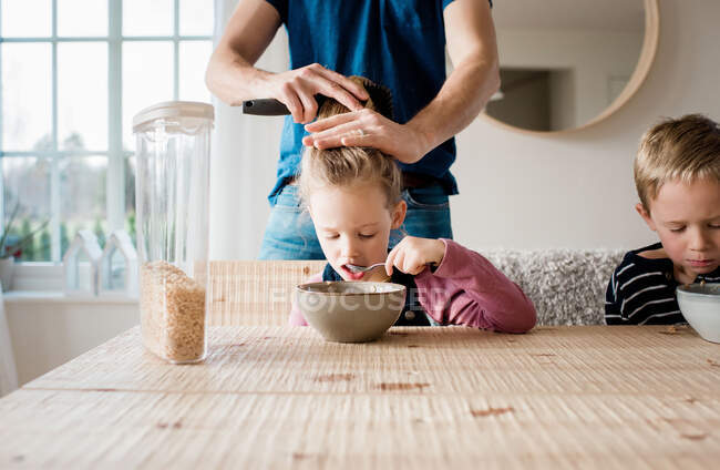 Father brushing his daughters hair whilst eating breakfast — Stock Photo