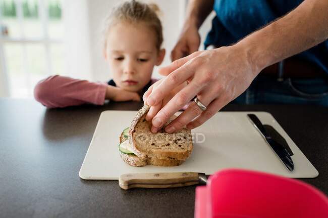 Батько робить своїм дітям упаковані обіди для школи, в той час як дочка дивиться — стокове фото