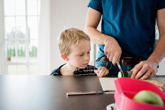 Vater macht seinen Kindern Lunchpakete für die Schule, während Sohn zuschaut — Stockfoto