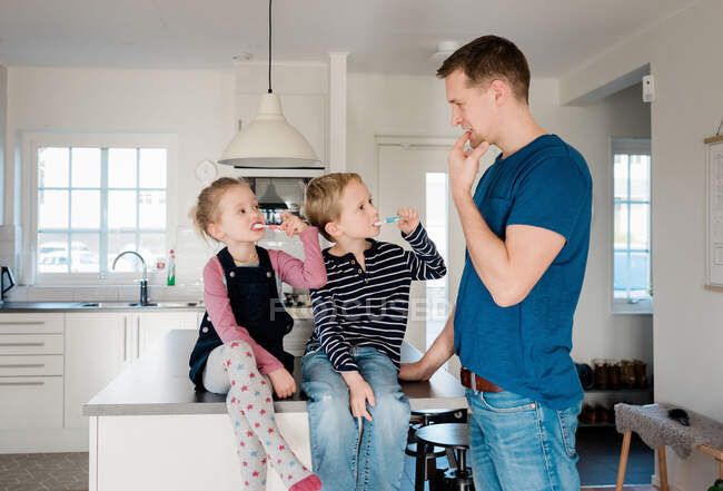 Padre mostrando a sus hijos cómo cepillarse los dientes antes de la escuela - foto de stock