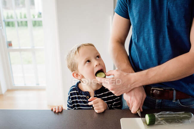 Father making his kids packed lunch whilst feeding his son for school — Stock Photo