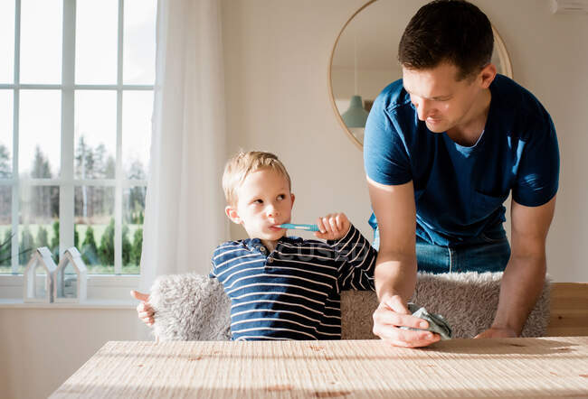 Young boy brushing his teeth looking at his dad before school — Stock Photo