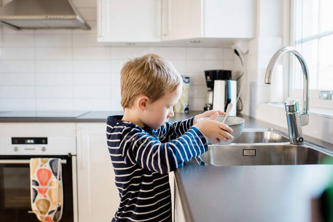 Молодий хлопчик допомагає з миттям після сніданку перед школою — стокове фото