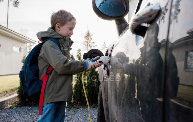 Jeune garçon branchant la voiture électrique familiale avant l'école — Photo de stock