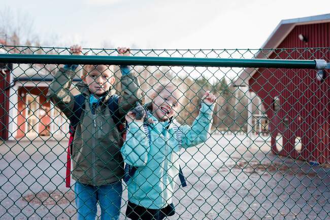 Fratelli guardando attraverso una recinzione scolastica sorridendo al loro padre — Foto stock