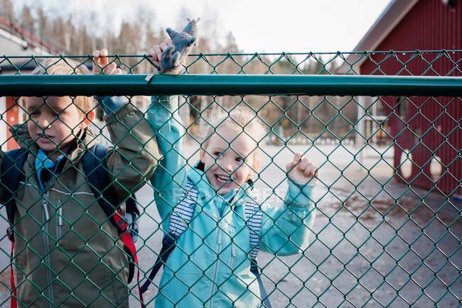 Niños mirando a través de una cerca de la escuela diciendo adiós a su padre - foto de stock