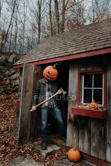 Uomo che indossa spaventosa testa di zucca intagliata nel capanno con ascia per Halloween. — Foto stock