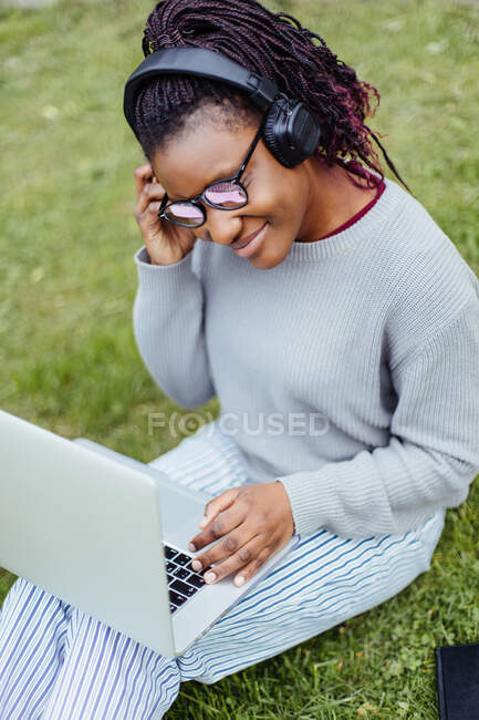 African American student using laptop and listening music on street — Stock Photo