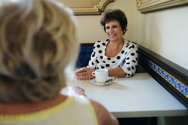 Frau lächelt beim Kaffee mit ihren Freunden und zeigt ihr Handy — Stockfoto