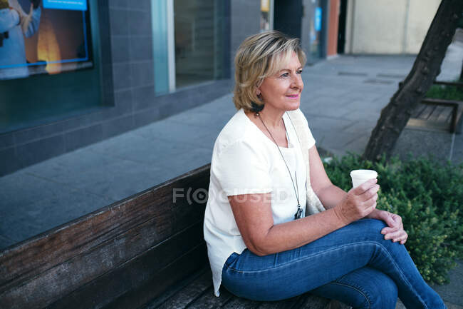 Woman drinking relaxed coffee enjoying the view on a bench in the stre — Stock Photo