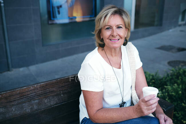 Señora sentada en el banco sonriendo sobre un café - foto de stock
