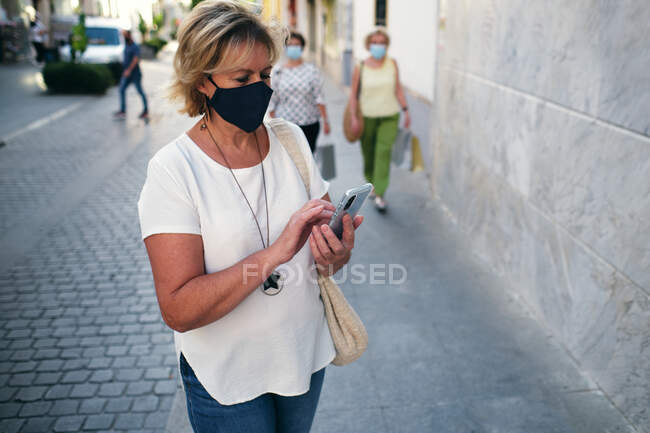 Donna che guarda il telefono e le donne che camminano con il loro shoppin — Foto stock