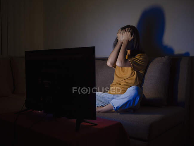 Young woman covering face with palms watching tv at night time — Stock Photo