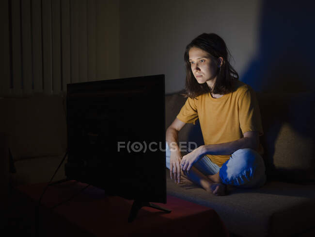 Молода жінка дивиться телевізор, сидячи поруч з екраном в нічний час — стокове фото