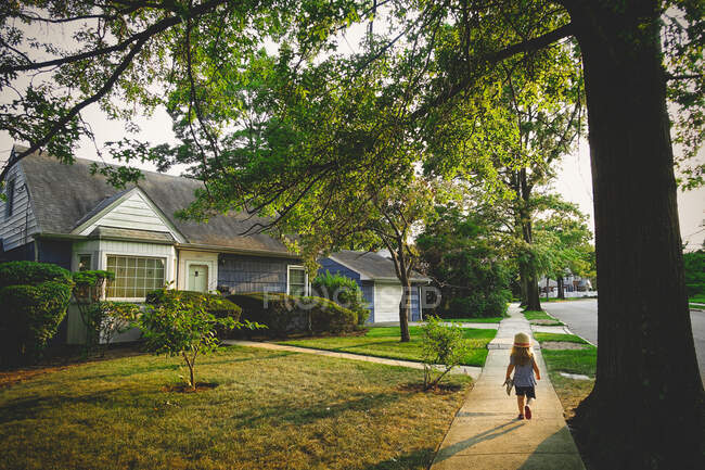 Ein kleines Mädchen geht auf einem Weg an einem blauen Haus vorbei. — Stockfoto