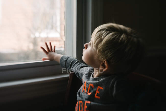 Un niño pequeño mira por una ventana. - foto de stock