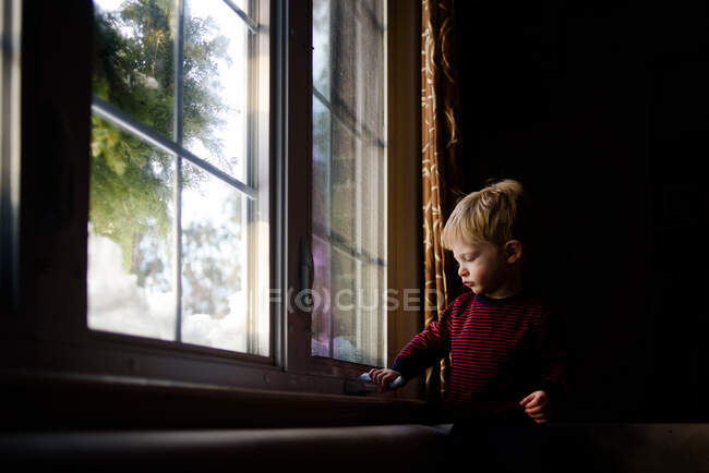 A little boy tries to open a window. — Stock Photo