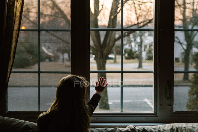 A little girl touches her living room window. — Stock Photo