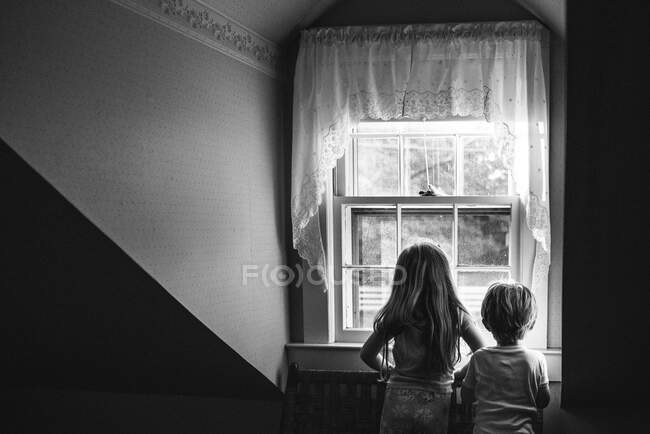 Duas crianças olham por uma janela. — Fotografia de Stock
