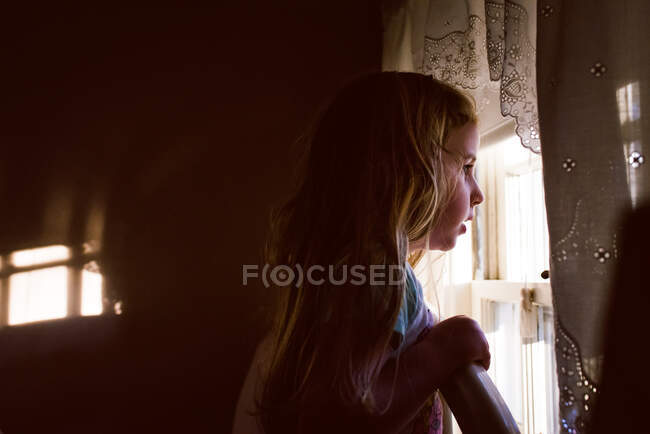 Una bambina guarda fuori dalla finestra di una camera da letto. — Foto stock