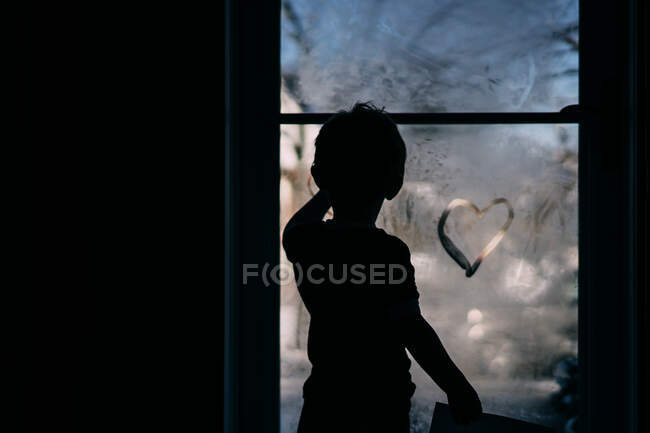 A little boy draws a heart on a foggy storm door. — Stock Photo