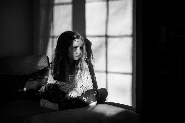 Ein kleines Mädchen sitzt im Schatten eines Fensters. — Stockfoto