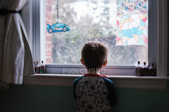 Un petit garçon regarde par la fenêtre dans sa chambre. — Photo de stock