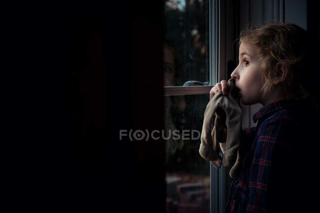 Una bambina che si succhia il pollice guarda fuori dalla porta principale. — Foto stock