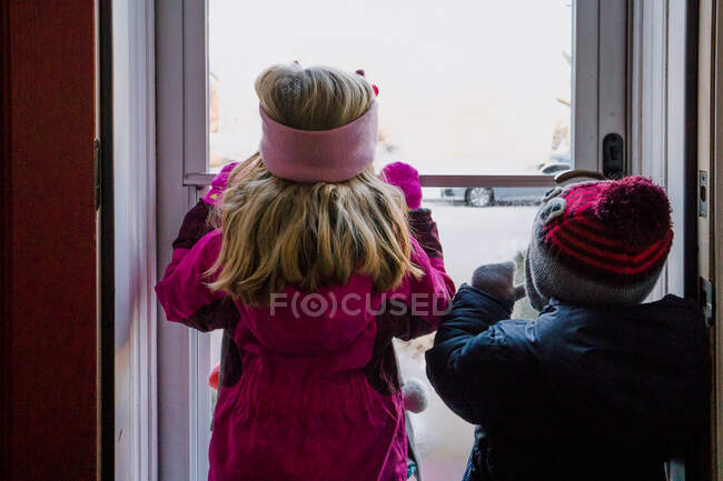 Zwei Kinder in Winterkleidung blicken durch eine Tür in den Schnee. — Stockfoto