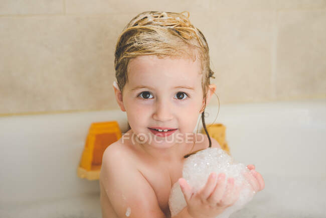 Una niña sostiene algunas burbujas en el baño. - foto de stock
