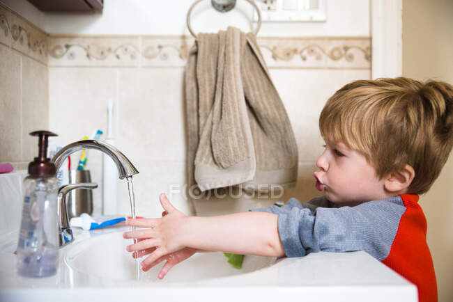 Un petit garçon se lave les mains dans l'évier de la salle de bain. — Photo de stock