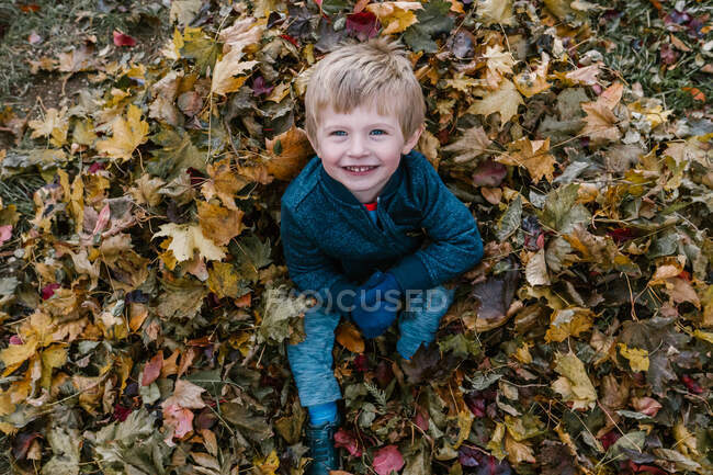 Un bambino siede in un mucchio di foglie. — Foto stock