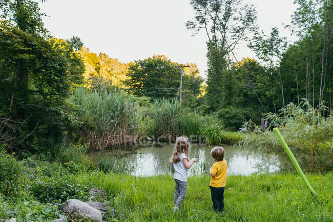 A boy and girl look out at a pond. — Stock Photo