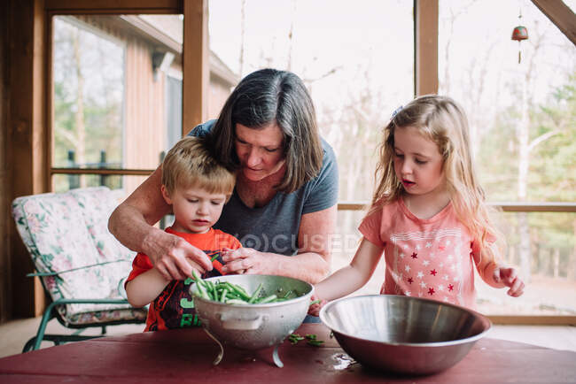 A grandmother teaches her grandchildren to snap green beans. — Stock Photo