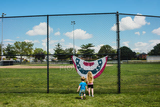 Dos niños están junto a una bandera en un campo de béisbol. - foto de stock