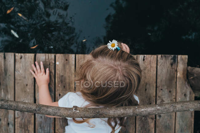 A little girl with a daisy in her hair lies on a pier. — Stock Photo