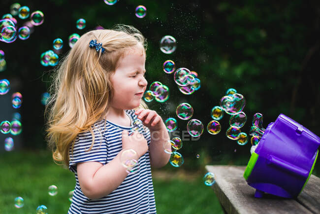 Una niña está parada frente a una máquina de burbujas. - foto de stock