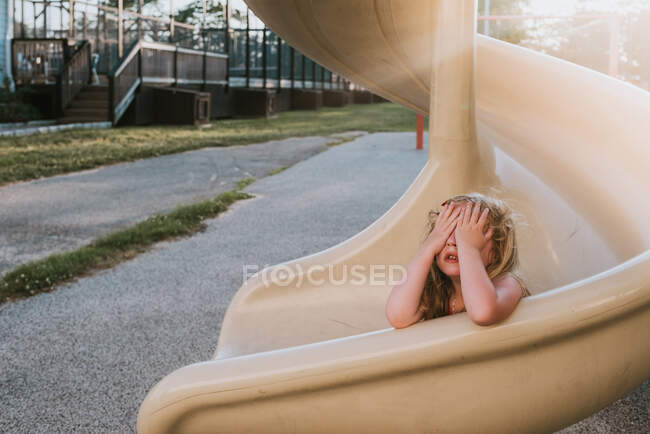 A little girl plays hide and seek on a slide. — Stock Photo