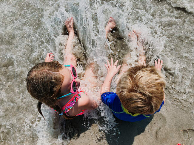 A boy and a girl sit in the surf at the beach. — Stock Photo