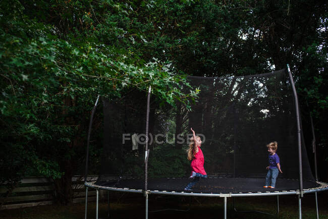 Uma menina e menino saltar em um trampolim ao ar livre. — Fotografia de Stock