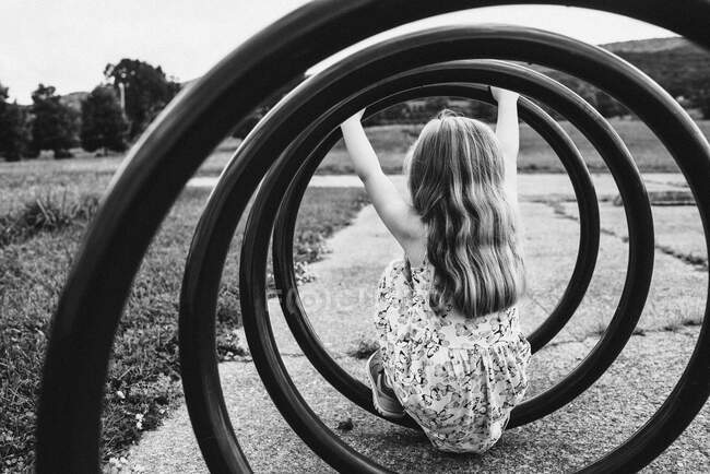 A little girl sits inside a spiral bicycle rack. — Stock Photo
