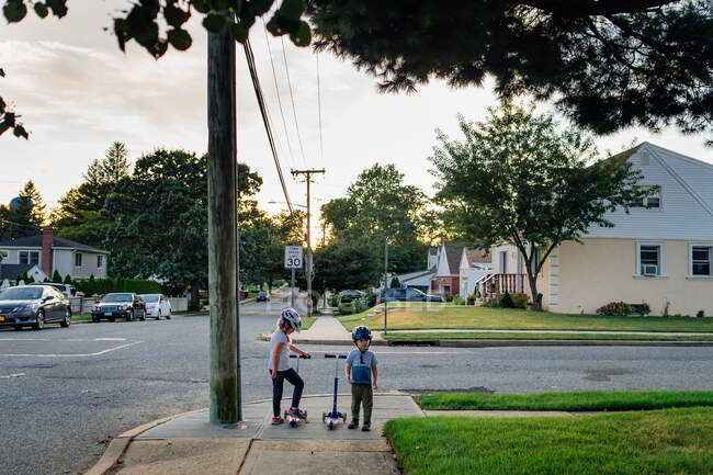 Two children stand on a street corner with their scooters. — Stock Photo
