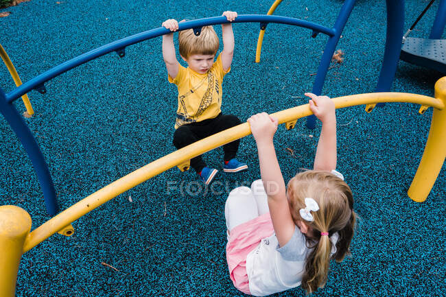 Dos niños se balancean en una estructura de patio. - foto de stock