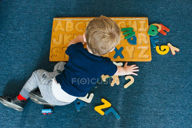 Um menino brinca com um quebra-cabeça alfabeto. — Fotografia de Stock
