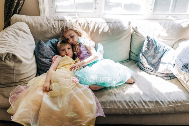 Хлопчик і дівчинка, одягнені в сукні принцеси, сидять на дивані . — стокове фото