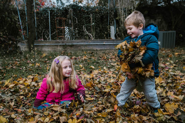 Two children play in a pile of leaves. — Stock Photo
