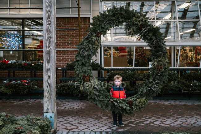 A little boy stands behind a huge wreath. — Stock Photo