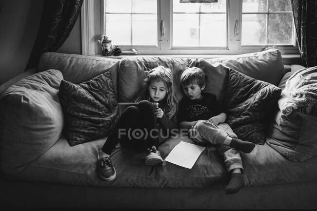 Dos niños juegan con una tableta en un sofá. - foto de stock