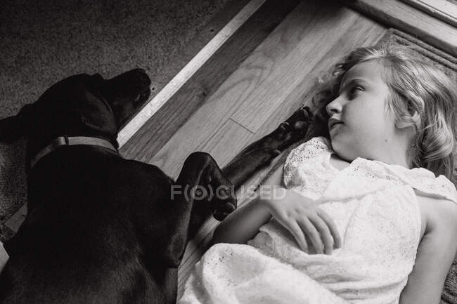 Ein kleines Mädchen liegt auf dem Boden neben ihrem schwarzen Hund. — Stockfoto